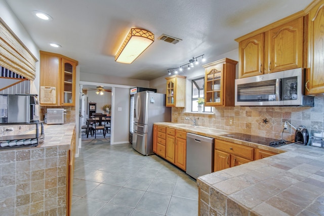 kitchen with stainless steel appliances, glass insert cabinets, tasteful backsplash, and light tile patterned flooring