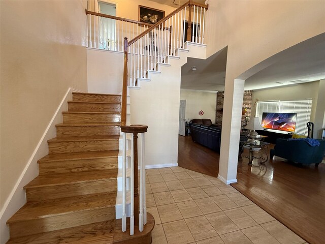 staircase with baseboards, a glass covered fireplace, a towering ceiling, and tile patterned flooring