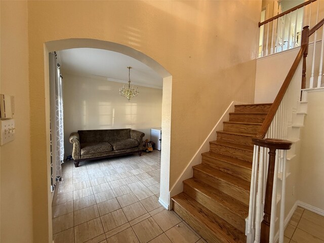 stairs with arched walkways, a chandelier, tile patterned floors, and baseboards