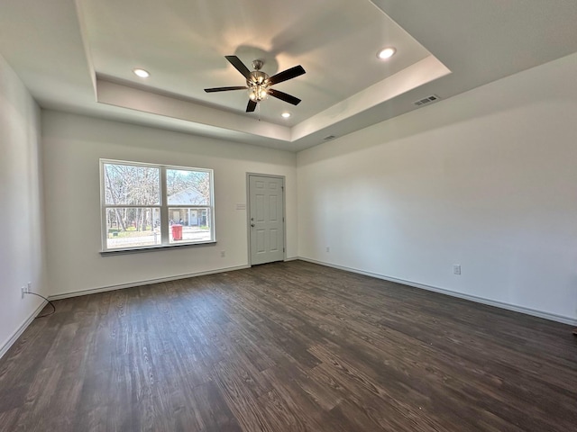 empty room featuring dark wood-style floors, baseboards, visible vents, ceiling fan, and a raised ceiling