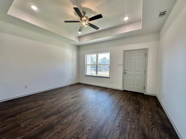 unfurnished room with visible vents, a raised ceiling, baseboards, and dark wood-style flooring