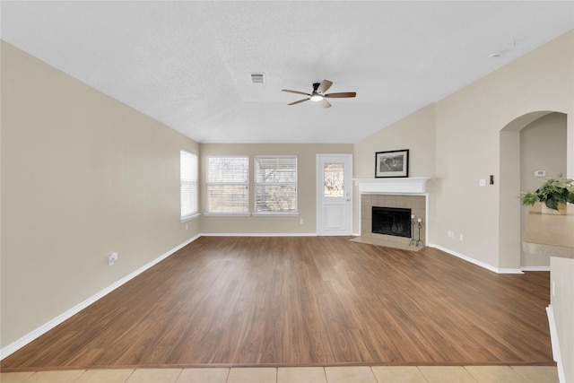 unfurnished living room featuring wood finished floors, a ceiling fan, a fireplace, vaulted ceiling, and a textured ceiling