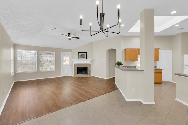 kitchen with visible vents, a tiled fireplace, open floor plan, light tile patterned floors, and ceiling fan with notable chandelier