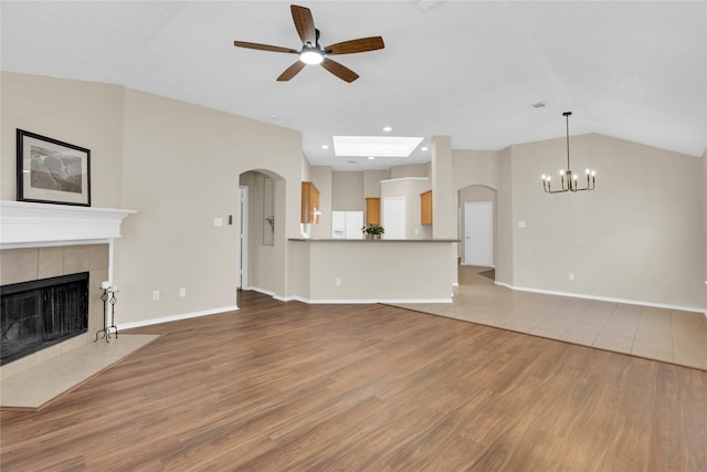 unfurnished living room with a tiled fireplace, lofted ceiling, wood finished floors, and baseboards