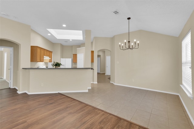 kitchen featuring visible vents, lofted ceiling, white refrigerator with ice dispenser, light wood-style floors, and under cabinet range hood