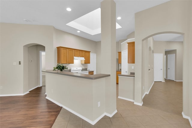 kitchen with light tile patterned floors, a skylight, recessed lighting, electric stove, and under cabinet range hood