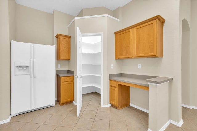 kitchen featuring light tile patterned flooring, brown cabinetry, baseboards, and white fridge with ice dispenser