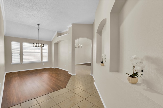 interior space with light tile patterned floors, an inviting chandelier, lofted ceiling, arched walkways, and a textured ceiling