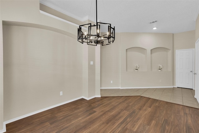 empty room with wood finished floors, visible vents, baseboards, a textured ceiling, and a notable chandelier