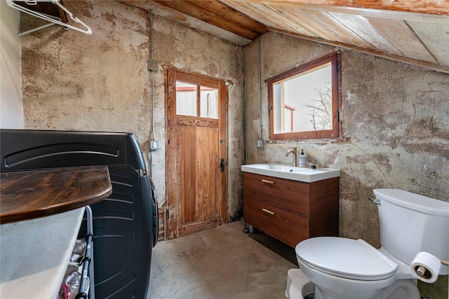 bathroom with toilet, concrete floors, vanity, and vaulted ceiling