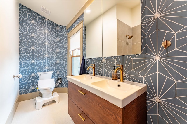 bathroom with vanity, baseboards, visible vents, wallpapered walls, and toilet