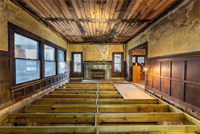 unfurnished living room with a wainscoted wall, wooden ceiling, and a fireplace