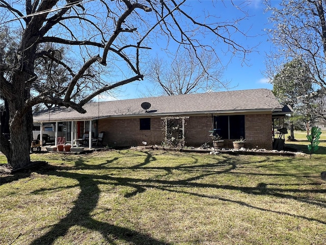 rear view of house with brick siding, a patio area, a shingled roof, and a yard