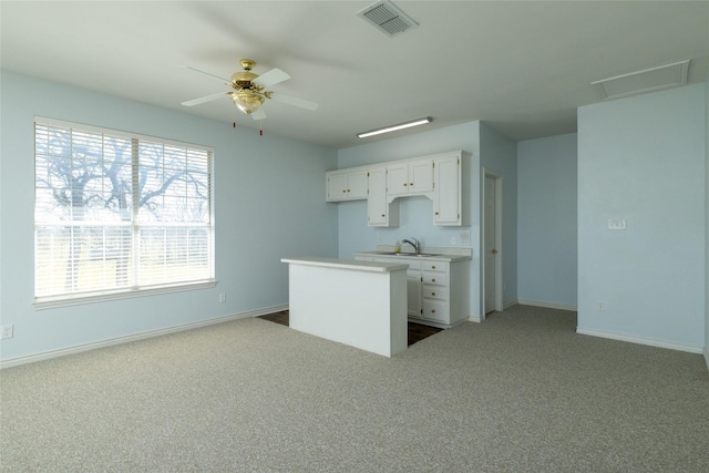 kitchen with visible vents, a kitchen island, light countertops, carpet floors, and white cabinetry