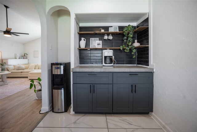 bar featuring marble finish floor, arched walkways, baseboards, ceiling fan, and vaulted ceiling