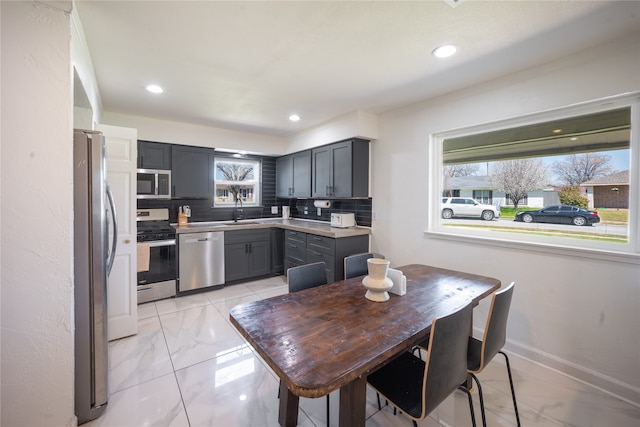 kitchen featuring gray cabinets, a sink, backsplash, appliances with stainless steel finishes, and baseboards