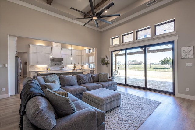 living area featuring visible vents, ceiling fan, baseboards, light wood-style floors, and a towering ceiling