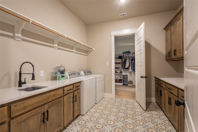 clothes washing area with light floors, visible vents, cabinet space, a sink, and independent washer and dryer