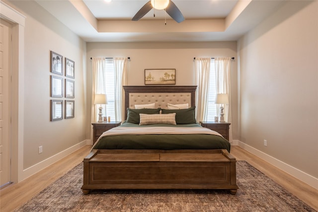 bedroom featuring a ceiling fan, a raised ceiling, baseboards, and wood finished floors