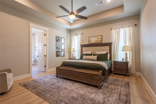 bedroom with a tray ceiling, light wood-style floors, visible vents, and baseboards