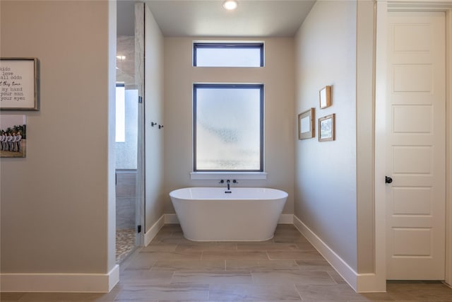 bathroom with baseboards, tiled shower, and a freestanding bath