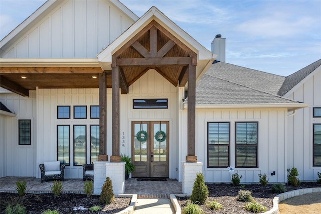 view of exterior entry featuring board and batten siding, a chimney, french doors, and roof with shingles