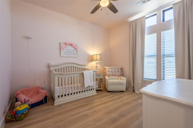 bedroom with visible vents, a crib, ceiling fan, and light wood finished floors