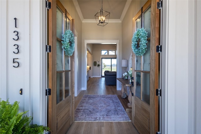 entryway with an inviting chandelier, wood finished floors, baseboards, and ornamental molding