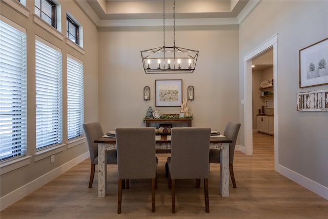 dining space featuring light wood-type flooring, baseboards, an inviting chandelier, and a towering ceiling