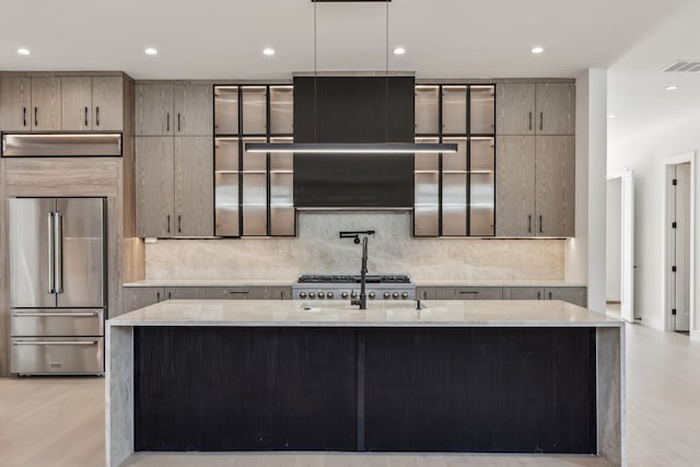 kitchen featuring light stone counters, visible vents, a kitchen island with sink, high quality fridge, and tasteful backsplash