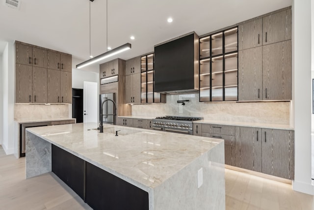 kitchen with tasteful backsplash, a spacious island, light stone counters, exhaust hood, and high end stainless steel range