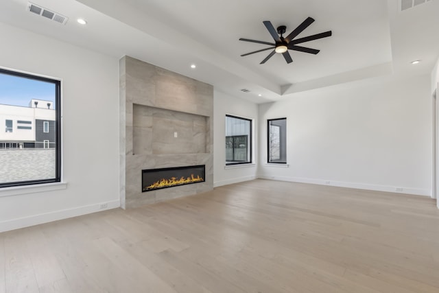 unfurnished living room featuring baseboards, a tile fireplace, wood finished floors, a raised ceiling, and a ceiling fan