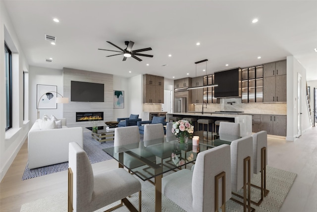 dining space with visible vents, a large fireplace, recessed lighting, light wood-style flooring, and a ceiling fan