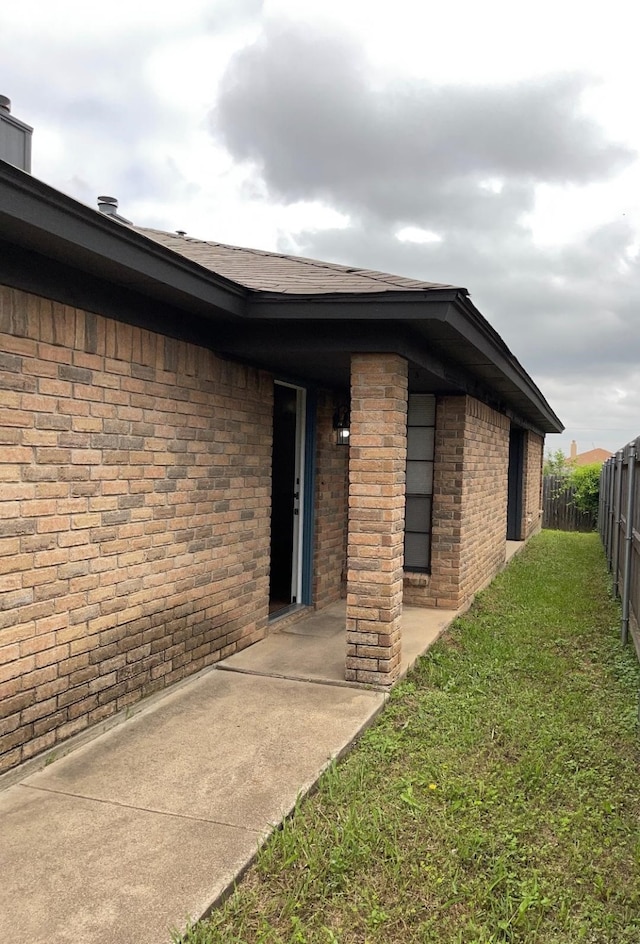 view of exterior entry with a yard, brick siding, and fence