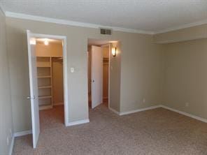 unfurnished bedroom with a walk in closet, visible vents, ornamental molding, a closet, and baseboards