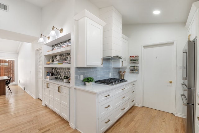 kitchen with light wood-style flooring, tasteful backsplash, stainless steel appliances, white cabinets, and light countertops