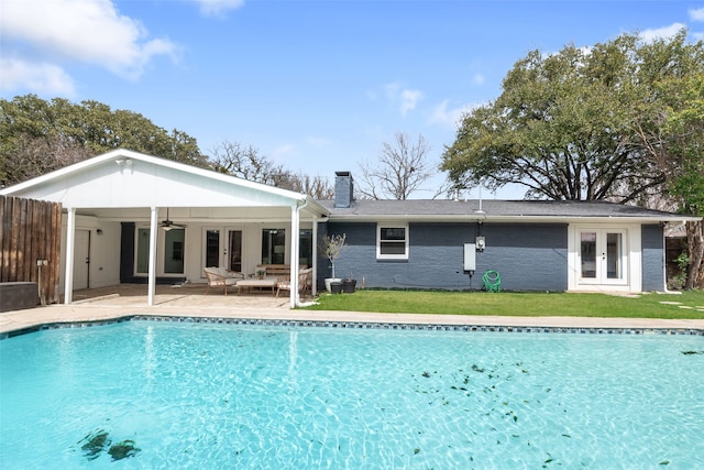 rear view of house featuring a ceiling fan, a yard, an outdoor pool, a chimney, and french doors