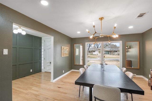 dining space with visible vents, baseboards, light wood-style floors, a decorative wall, and a notable chandelier