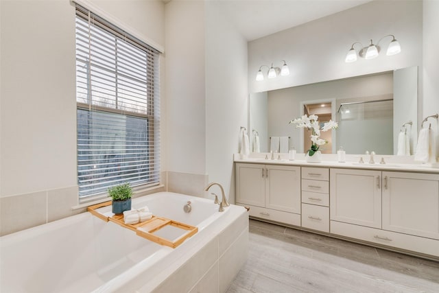 bathroom with double vanity, a bath, wood finished floors, and a sink