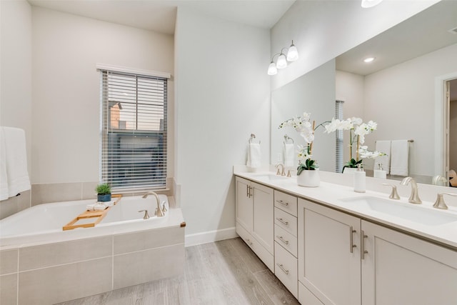 bathroom with double vanity, a bath, wood finished floors, and a sink