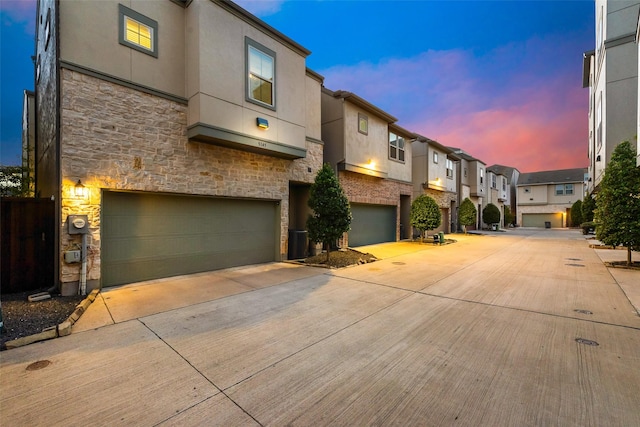 view of front of home with stucco siding, concrete driveway, a garage, stone siding, and a residential view