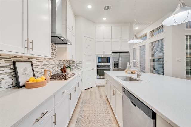 kitchen featuring visible vents, a sink, light countertops, appliances with stainless steel finishes, and wall chimney range hood