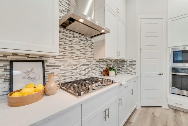 kitchen featuring decorative backsplash, wall chimney range hood, white cabinets, and appliances with stainless steel finishes