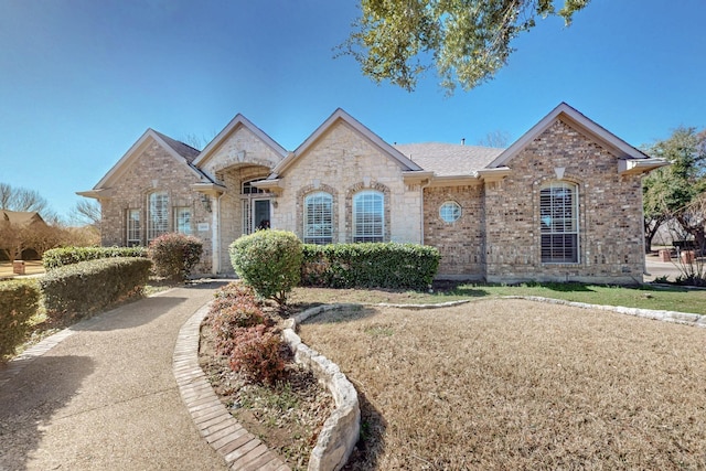 french country style house featuring brick siding and a shingled roof