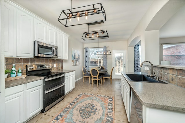 kitchen with light tile patterned floors, a wealth of natural light, arched walkways, stainless steel appliances, and a sink