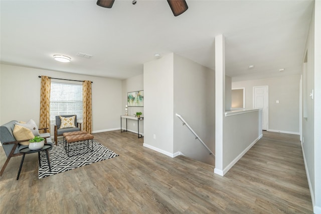 sitting room with visible vents, an upstairs landing, wood finished floors, baseboards, and ceiling fan