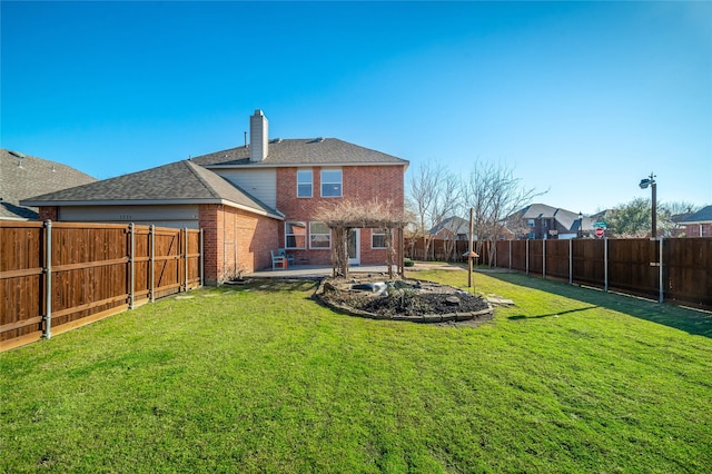 rear view of property with brick siding, a fenced backyard, a chimney, and a yard