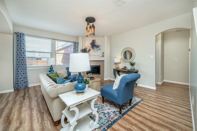 living area featuring arched walkways, a tiled fireplace, baseboards, and wood finished floors