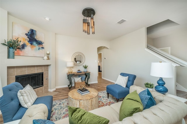 living room with visible vents, a tiled fireplace, wood finished floors, arched walkways, and baseboards