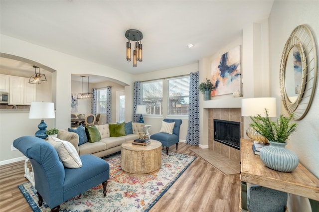 living room with arched walkways, a tile fireplace, light wood-type flooring, and baseboards